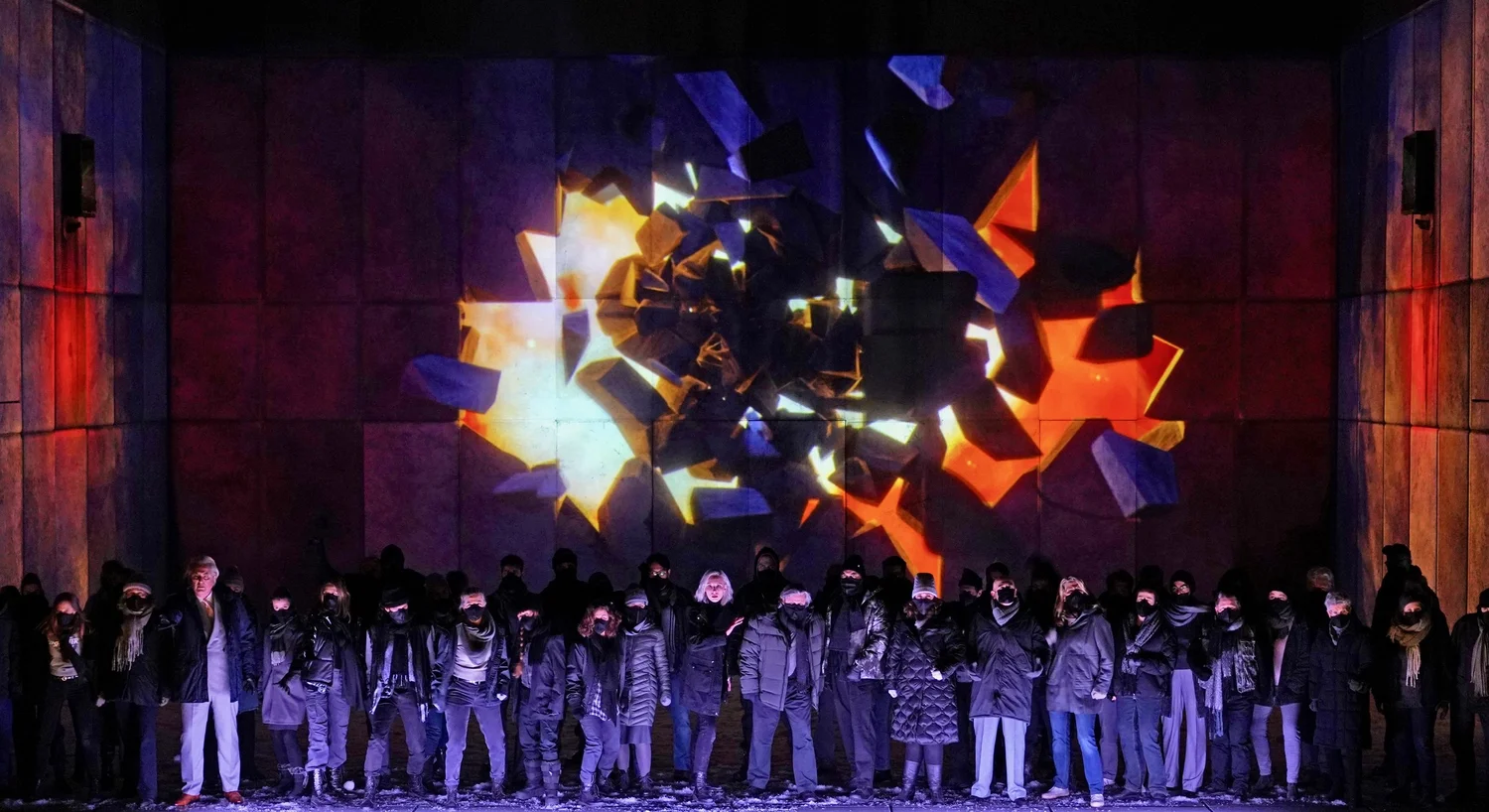 The NORMA chorus beneath a colourful projection of the fractured stage set.